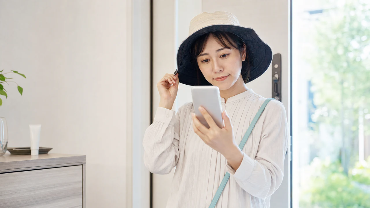 帽子で紫外線対策をしながらスマートフォンで再診予定を確認する女性
